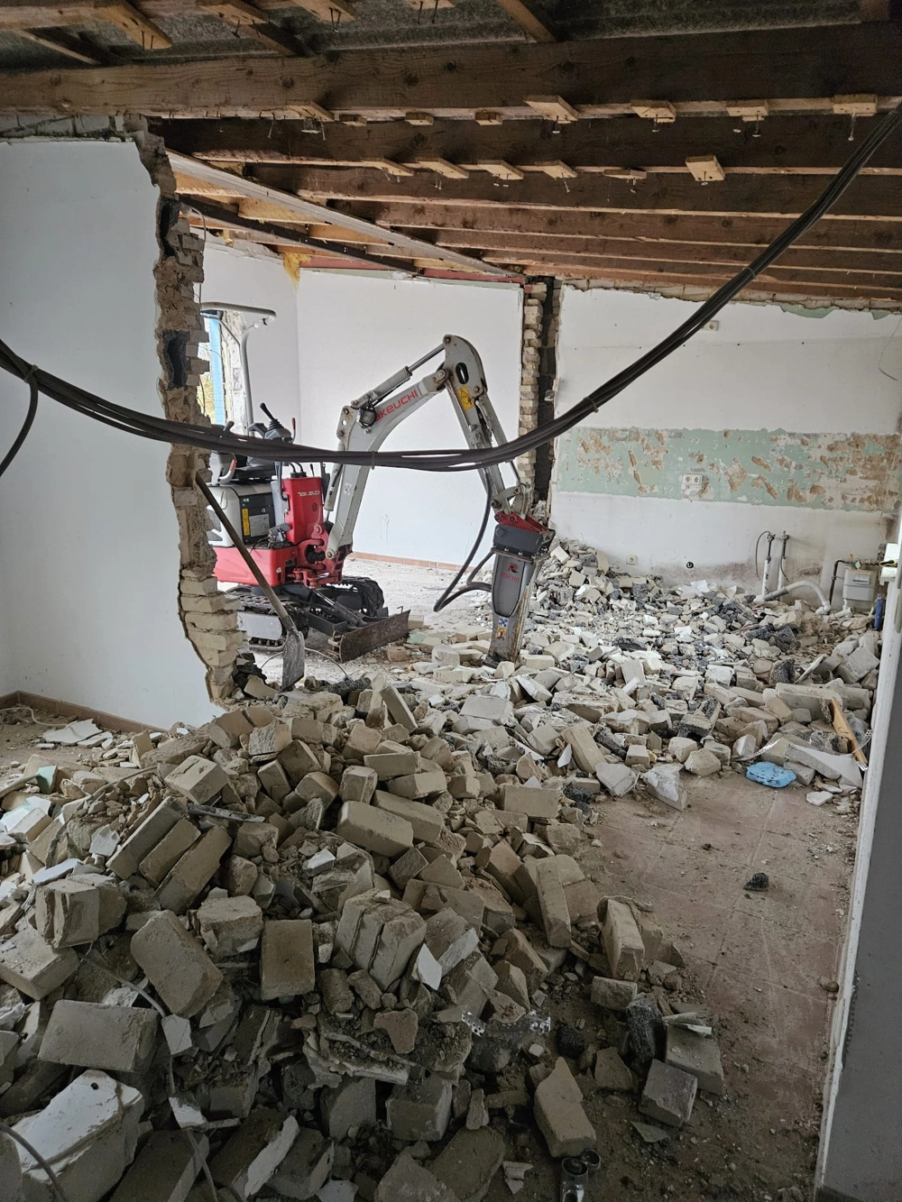 Innenraum mit Minibagger und Schutt während Wandabbruch im Rahmen einer Renovierung