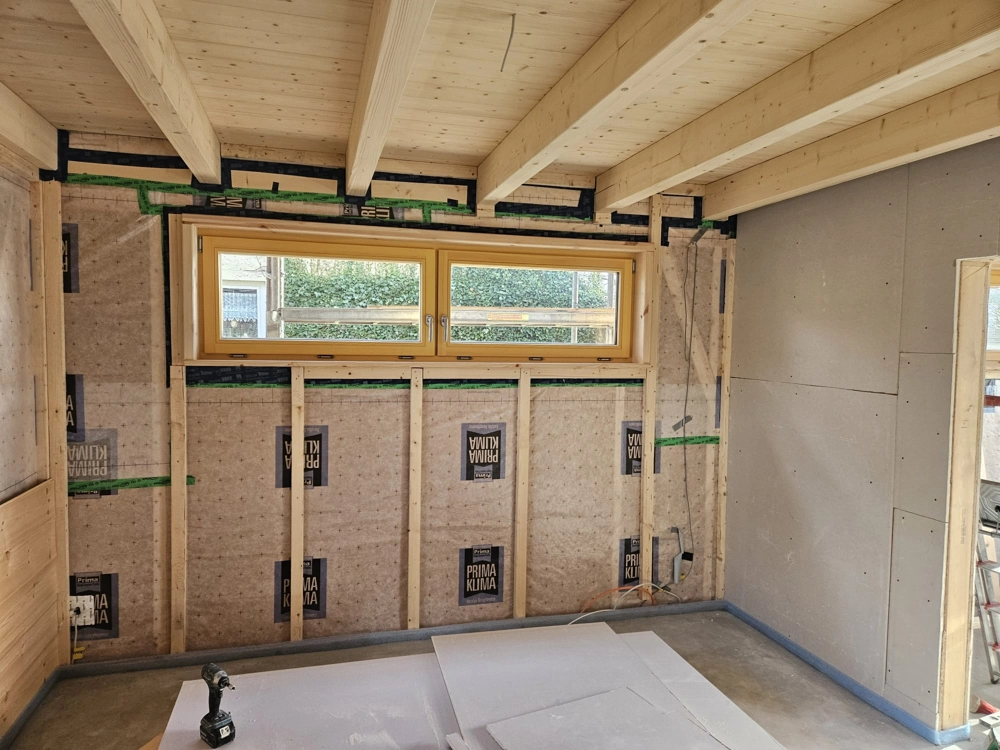 Innenraum mit Holzbalkendecke und offener Holzständerwand mit Dämmung im Trockenbau, sichtbare Kabel und Bohrschrauber