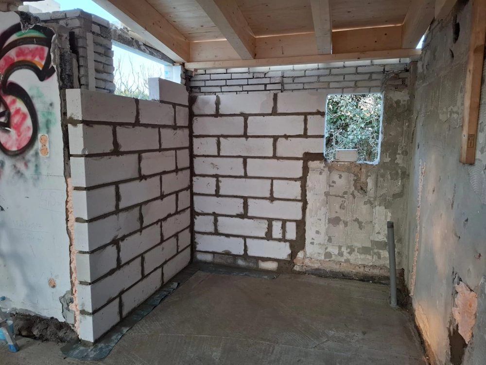 Zimmer mit halbfertigen Trockenbauwänden aus Porenbetonblöcken und sichtbarer Holzdecke während Innenausbau