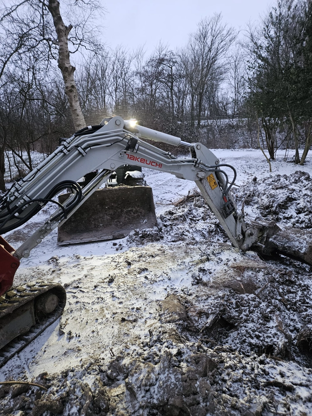 Kompakter Bagger bei Erdarbeiten im verschneiten Gartenbereich