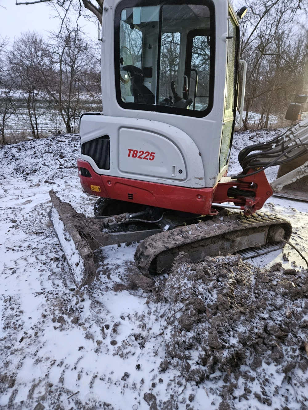 Kompakter Minibagger im Einsatz für Erdarbeiten auf verschneitem, matschigem Baustellengelände