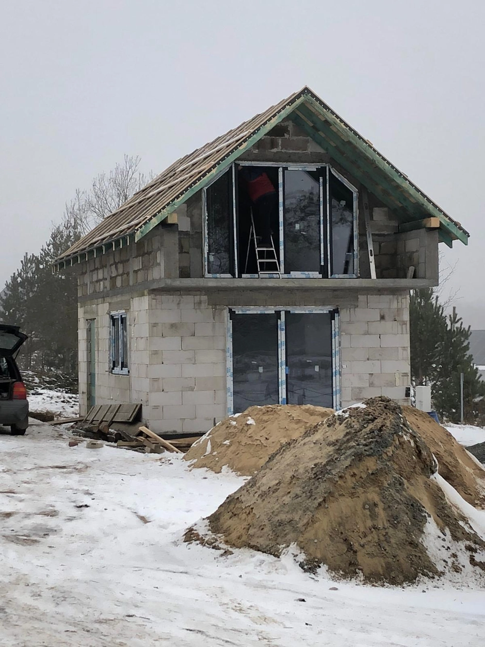 Rohbau eines zweistöckigen Einfamilienhauses mit Betonblockmauerwerk, Fensteröffnungen und Sandhaufen, Generalunternehmer