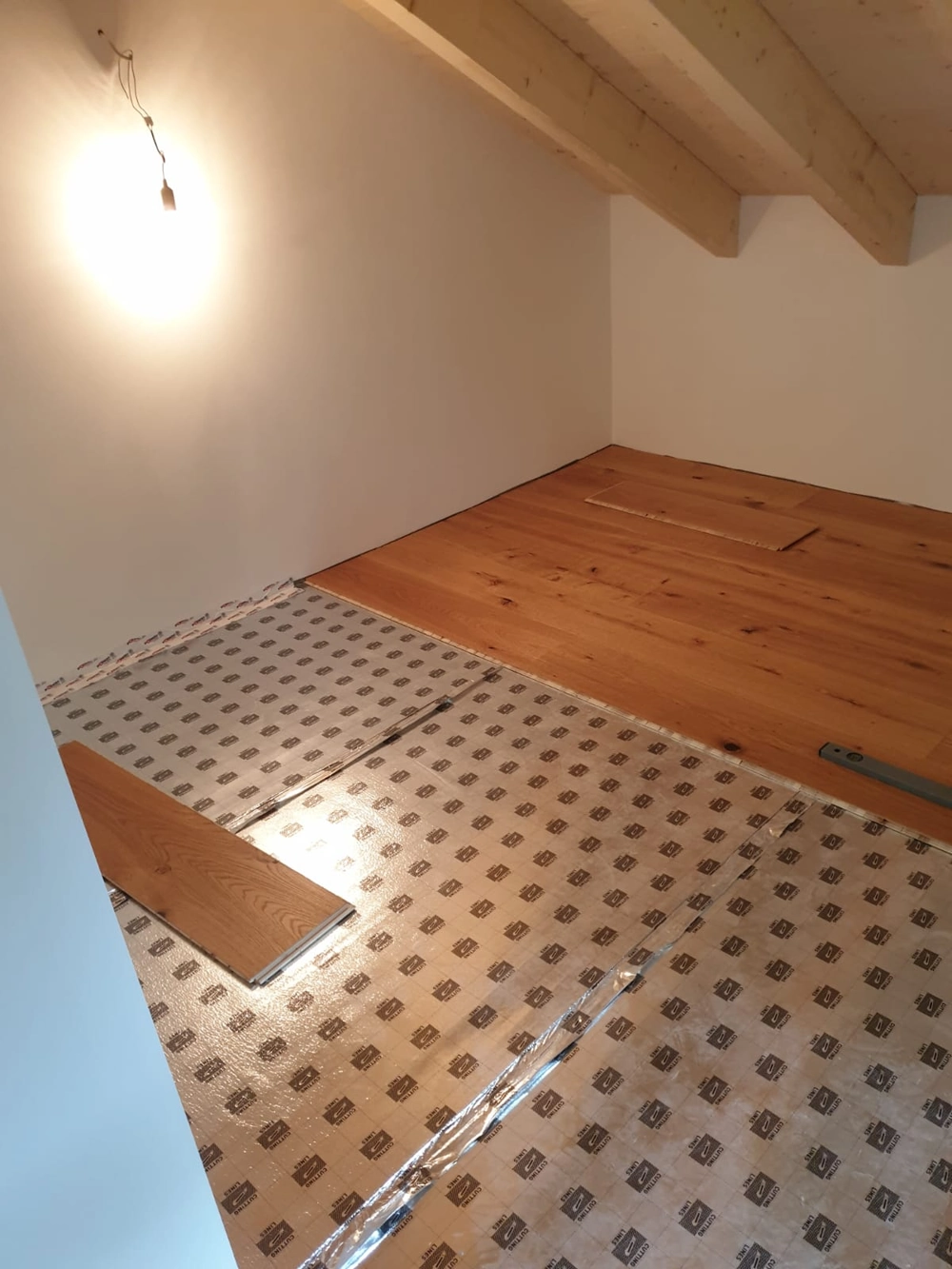 Parkett verlegen: halb verlegter Eichendielenboden auf Dämmunterlage in Dachgeschoss mit nackter Lampe