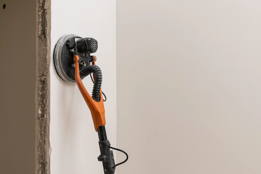 Spachtelarbeiten: Elektrische Wandschleifmaschine glättet gespachtelte Trockenbauwand
