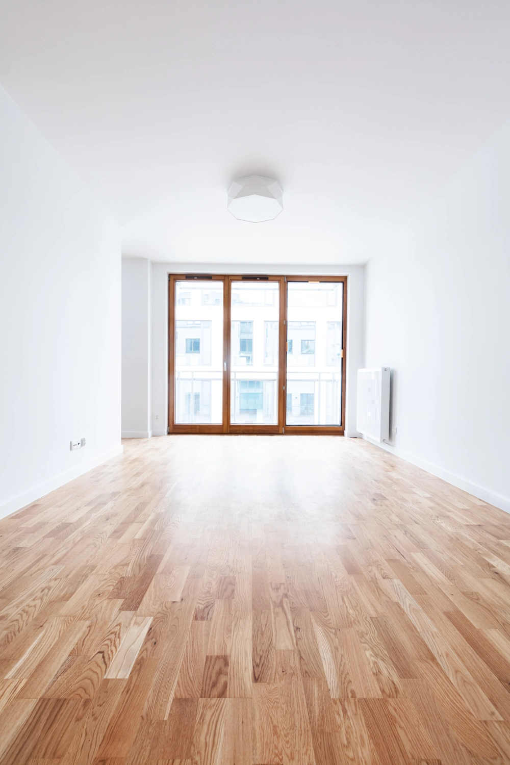 Leerer Raum mit neu verlegtem Parkettboden und großen Fensterfronten