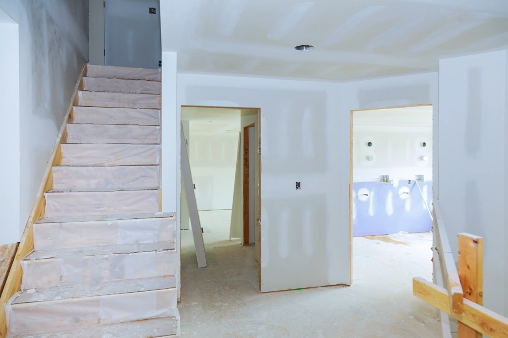 Rohbau-Innenraum mit gespachtelten Trockenbauwänden, geschützter Holztreppe und offener Tür