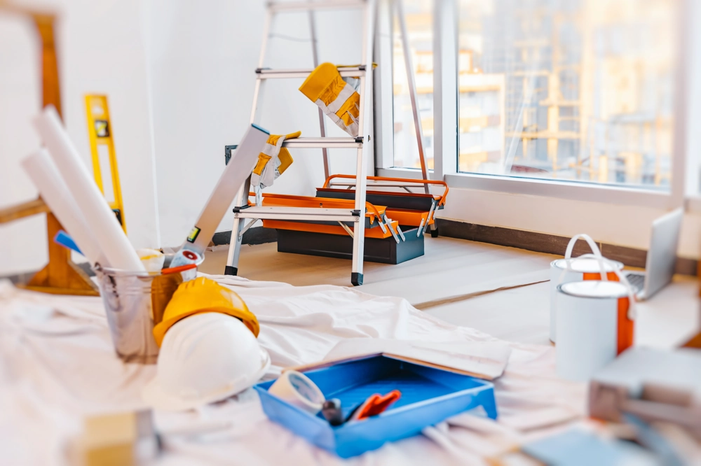 Vorbereitungen für Malerarbeiten: Leiter, Farbeimer, Malerrolle und Bodenschutz im Zimmer