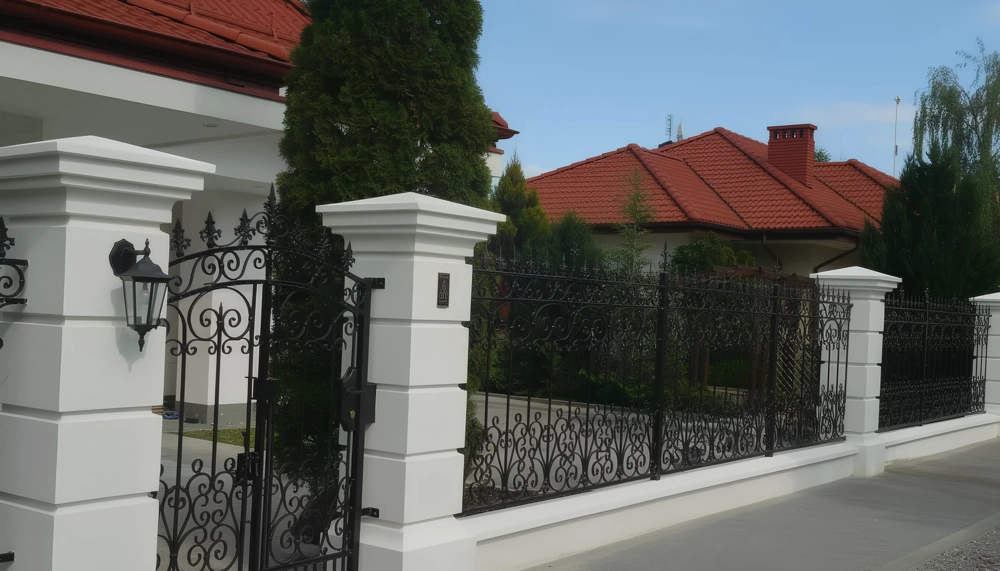 Zäune ornamentaler schmiedeeiserner Zaun mit weißen Stützpfeilern und Eingangstor vor Wohnhaus