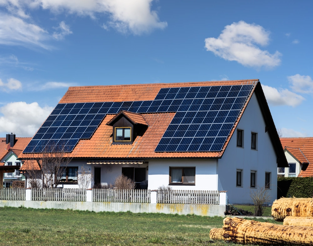 Wohnhaus mit Photovoltaik montage auf rotem Ziegeldach, weiß verputzte Fassade und grünem Vorgarten