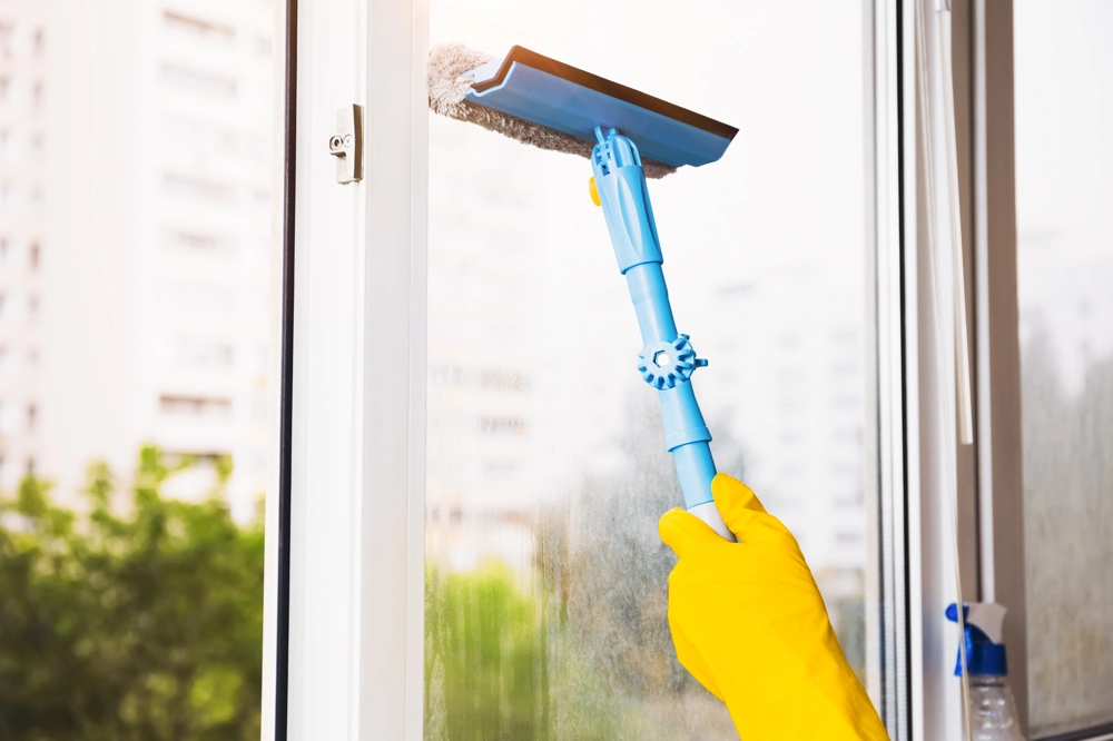 Fensterreinigung: Hand mit gelben Gummihandschuhen reinigt Glasfenster mit Teleskopwischer