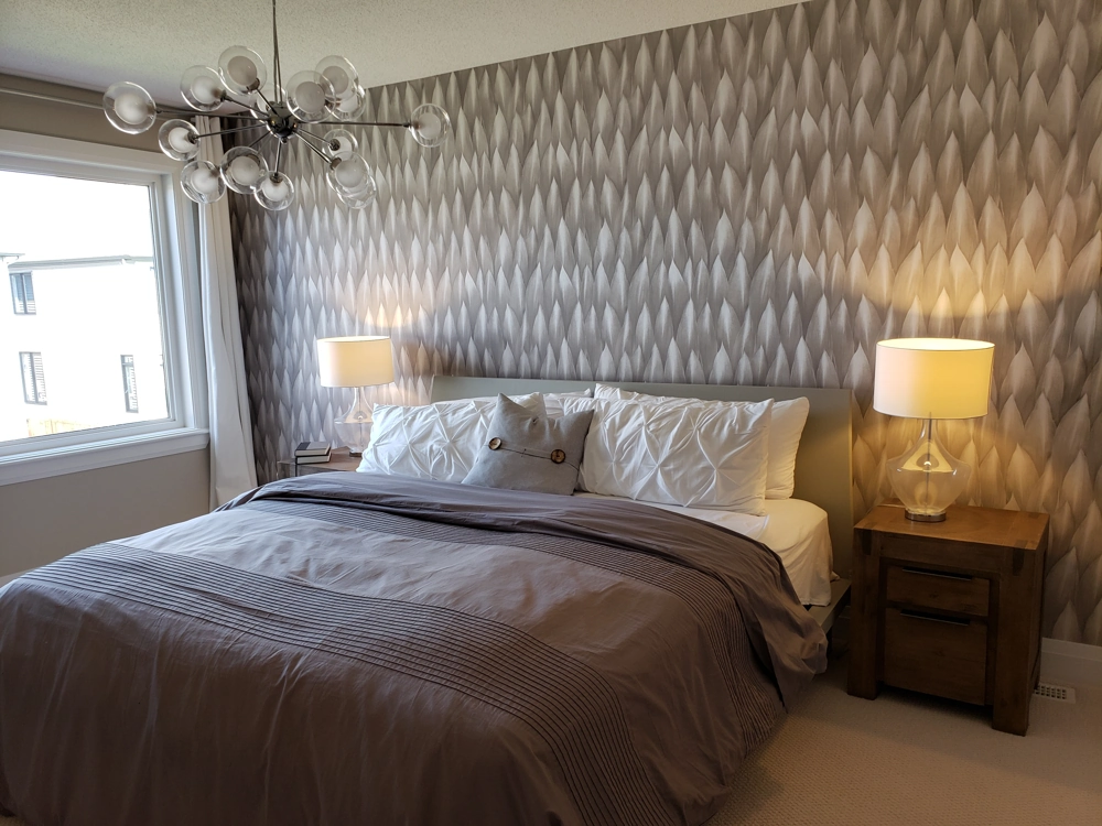 Schlafzimmer mit gemusterten Tapezierarbeiten an Wand, Doppelbett mit Nachttischlampen und modernem Deckenleuchter