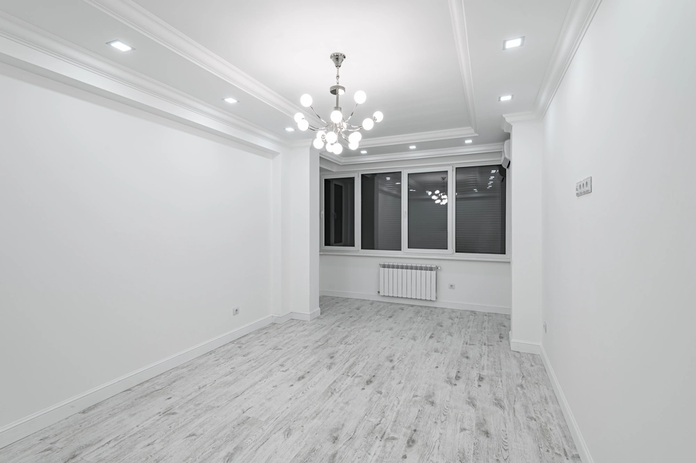 Renovierter Raum mit weißen Wänden, LED-Deckenleuchten, Kronleuchter und hellgrauem Boden nach Laminat verlegen