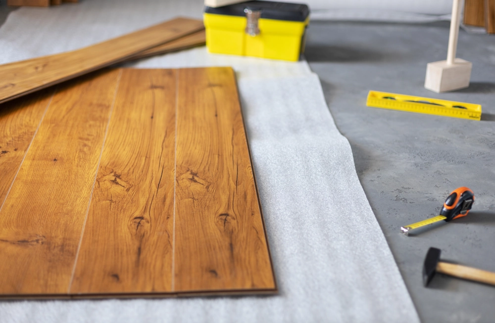 Laminat verlegen: Holzlaminatplatten auf Unterlage mit Hammer, Wasserwaage, Maßband und Werkzeugkiste