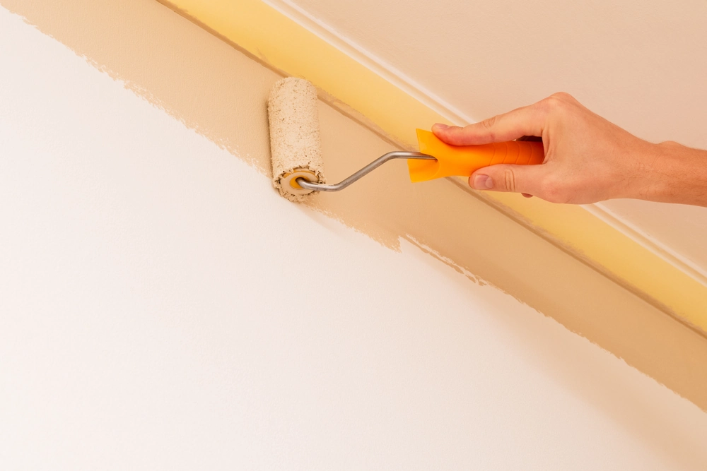 Malerarbeiten: Farbrolle gleitet am Deckenübergang, Wand in hellem Beige präzise gestrichen