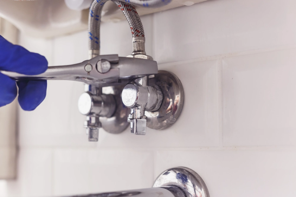 Hand mit Rohrzange montiert Eckventile der Sanitärinstallation an gefliester Wand