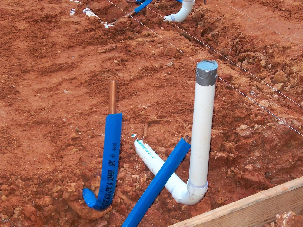 Verlegte weiße PVC-Leitungen und isolierte Kupferrohre in Baugrube zur Sanitärinstallation