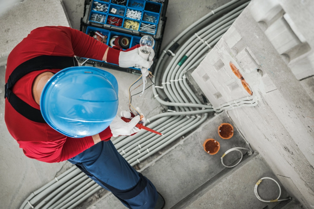 Handwerker mit Helm installiert Leuchtmittel und verbindet Kabel bei Elektroinstallationen
