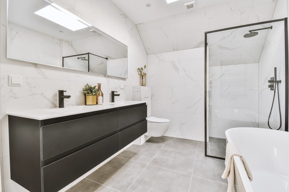 Modernes Badezimmer nach Badsanierung mit freistehender Badewanne, begehbarer Dusche, Wand- und Bodenfliesen und schwarzem Doppelwaschtisch