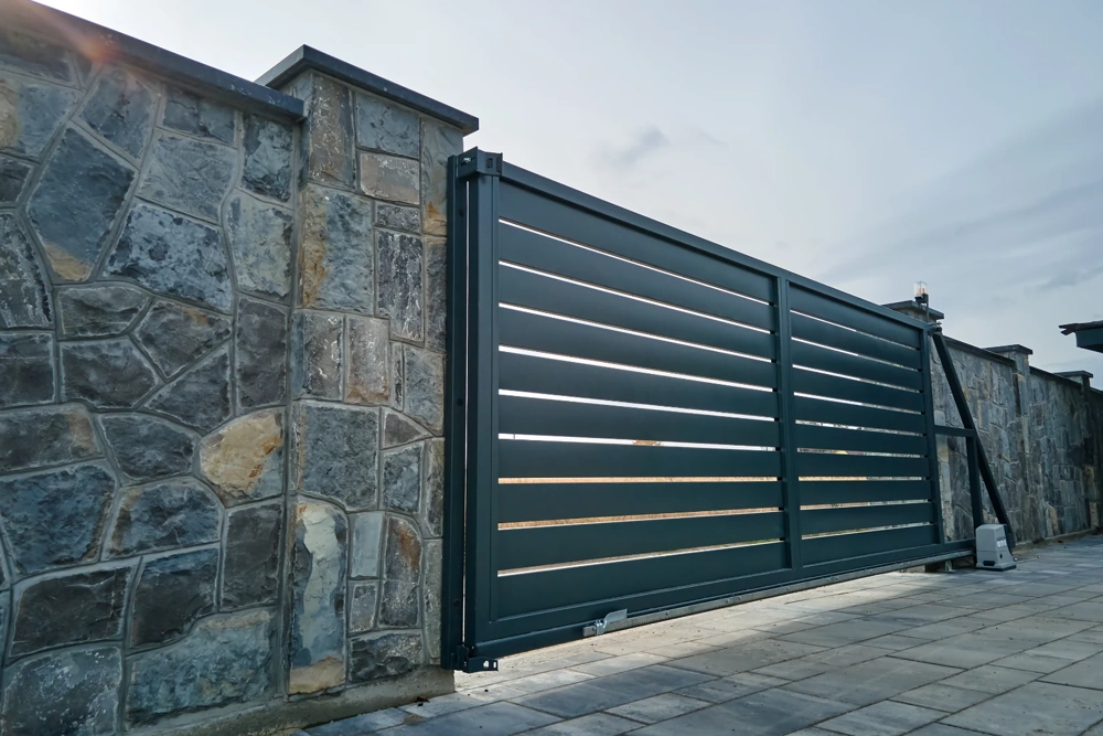 Moderner Metall-Schiebetor aus grau lackierten Lamellen als Zauninstallation vor Natursteinmauer