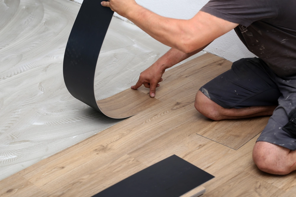Handwerker verlegt Vinylboden in Holzoptik auf verklebten Untergrund